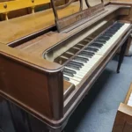 An old upright piano with damaged, missing, and uneven keys stands in a room with gray carpeting.