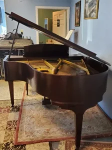 A brown grand piano is placed on a patterned rug in a room with light blue walls and framed pictures.