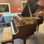 A brown grand piano with an open lid sits in a room, accompanied by a floral-patterned bench.