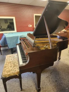 A brown grand piano with an open lid sits in a room, accompanied by a floral-patterned bench.
